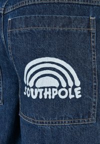 Denim jeans with a dark blue fabric. Features a white embroidered rainbow design and the text "SOUTHPLE" on the right back pocket.