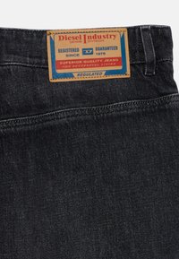 Jean en denim noir avec une étiquette en cuir. L'étiquette comprend "Diesel Industry", des détails d'enregistrement et un texte sur la qualité supérieure.