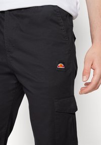 Svarta cargobyxor i slitstarkt tyg, med en sidficka och en liten broderad logo i röd och orange.