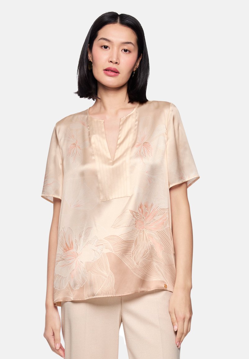 Satinbluse in sanftem Beige mit floralem Muster in Hellrosa. Mit V-Ausschnitt, kurzen Ärmeln und einem leichten Saumakzent am unteren Rand.
