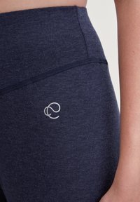 Marineblauwe hoogrenderende leggings van textiel hebben een klein zilveren logo op de dij, wat een eenvoudige en functionele uitstraling benadrukt.