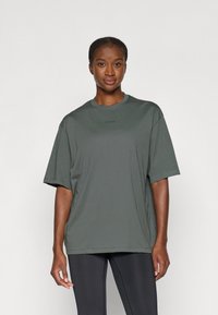 Tmavo zelené oversized tričko s krátkymi rukávmi, okrúhlym výstrihom a jemným logom na hrudi. Hladká tkanina s voľným strihom.