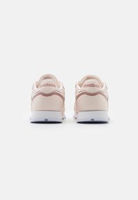 Rosa lädersneakers med en vit gummisula, som har en diskret Reebok-logotyp på hälen och en kontrasterande grå detalj på sidan.