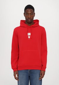Red cotton hoodie featuring a front pocket, drawstring hood, and a small graphic design in the center. Long sleeves with ribbed cuffs.