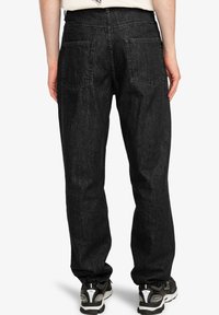 Pantalones de mezclilla negros con corte recto, bolsillos traseros y un acabado texturizado, combinados con zapatillas grises con acentos reflectantes.