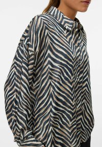 Silke skjorte med zebra-stripes mønster i beige, svart og hvitt. Knappelukking, kragehals og løs passform med oppbrettede ermer.