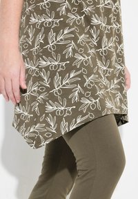 Tunique verte avec imprimé de branche d'olivier blanche, associée à des leggings olive. La tunique présente un ourlet arrondi et un tissu doux et texturé.