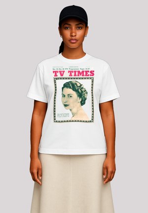 Woman wearing a black cap, white t-shirt with vintage "TV Times" magazine cover featuring a portrait of a woman with styled hair and a necklace.