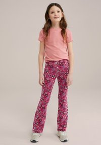 Top roz cu mâneci scurte, cu margini volănașe, asortat cu pantaloni evazați cu imprimeu floral în nuanțe de roz, alb și negru. Tenisi albi.