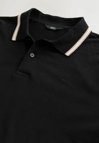 Black polo shirt made of textured fabric, featuring a two-button placket, a thin striped collar in beige, and an embossed logo on the chest.