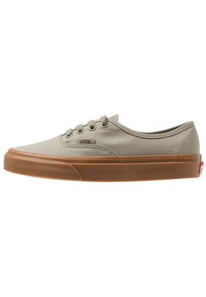 Zapatilla beige de lona baja con suela de goma marrón, cierre de cordones y pequeño logo de Vans en el lateral.