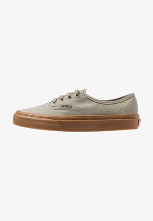 Zapatilla beige de lona baja con suela de goma marrón, cierre de cordones y pequeño logo de Vans en el lateral.
