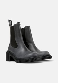 Botas Chelsea de cuero gris con paneles laterales elásticos y una suela de goma negra gruesa que presenta profundos surcos para mayor agarre.