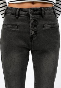 Black denim high-waisted pants with five-button closure, front pockets, and a smooth texture. Features a fitted design and slight fade.