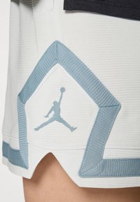 Hvide basketballshorts med tekstureret stof, blå kant og et trykt blåt Jumpman-logo i nederste venstre hjørne.