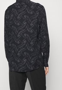 Zwart shirt met een herhalend wit tijgerpatroon, met lange mouwen, een afgeronde zoom en een zachte, gestructureerde stof.