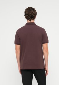 Pánská polokošile s krátkým rukávem v tmavě švestkové barvě, vyrobená z bavlny, s klasickým límečkem a jemnou značkovou štítkem na spodním lemu. Hladká textura.