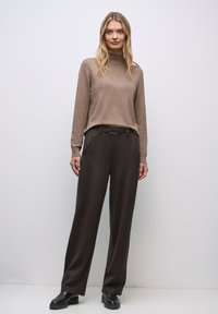 Brun polo-tröja ihop med mörkbruna vida byxor. Stilig spänne detalj på bältet, slät tygstruktur och minimala accessoarer.