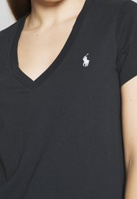 Femmes portant un t-shirt noir à col en V avec un petit logo de joueur de polo blanc sur la poitrine gauche.