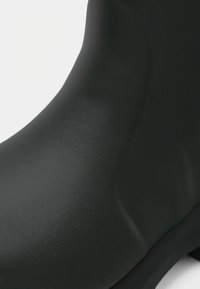 Juodos gumines botago su lygiu paviršiumi, apvalia forma ir subtiliu dizainu, kuris turi pakeltą siūlę ties kulkšnimi.