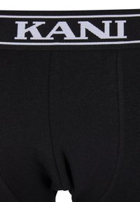Boxerii din bumbac negri cu un logo alb KANI pe talie. Au o textură netedă și o potrivire strânsă, fără cusături vizibile.
