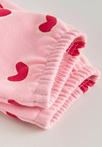 Rosa stickade sweatpants med mönster av röda chilifrukter, utrustade med elastiska muddar och mjuk textur.