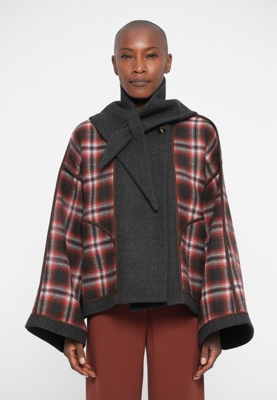 Cappotto di lana a quadri in rosso, nero e bianco con una sciarpa di lana grigia. Presenta maniche ampie e una chiusura con bottoni, con bordature a contrasto.