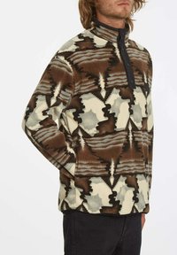 Pull en polaire avec un motif abstrait multicolore dans des tons de marron, crème et vert. Il possède un col monté et une fermeture à boutons à l'avant.