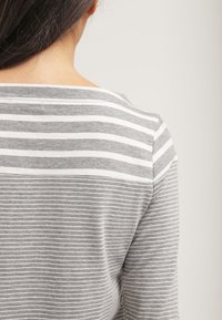 Haut rayé gris et blanc avec un col bateau, fabriqué en tissu doux. Présente des lignes horizontales étroites et une coupe décontractée.