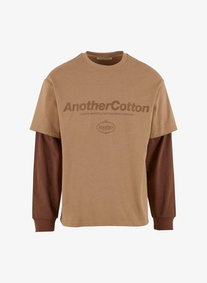 Heled pruun puuvillane T-särk, mille all on tumepruuni värvi pikad varrukad. Esiküljel on suur logo tumedates pruunides tähtedes.