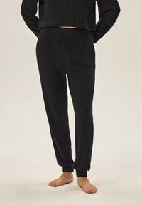 Czarny dzianinowy zestaw do wypoczynku z krótkim topem i spodniami na elastycznym pasie, oba z dopasowanymi mankietami. Miękka tekstura materiału.