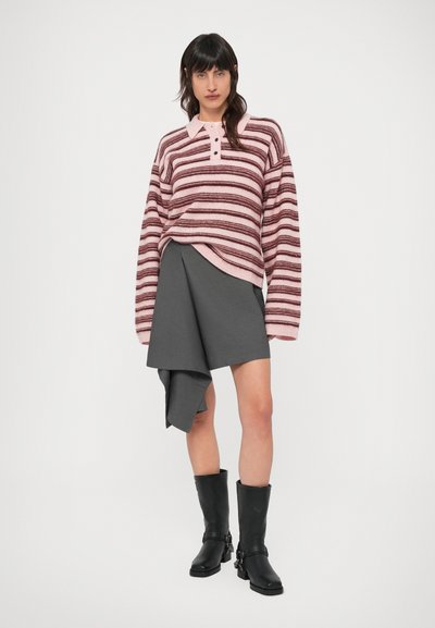 Ριγέ πλεκτό πουλόβερ σε ροζ και βουργουνδί, με γιακά και κουμπιά. Συνδυάζεται με γκρι ασύμμετρη φούστα και μαύρες μπότες που φτάνουν ως το γόνατο.