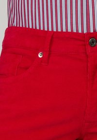 Rode corduroy broek met een voorvak, metalen knoopsluiting en verticale ribbelstructuur.