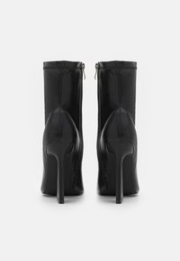 Bottines à talons hauts noires en cuir avec fermeture éclair et détails cousus. Texture lisse et design épuré.