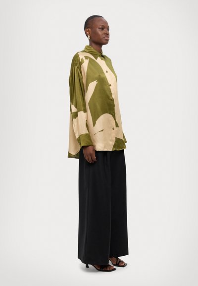 Green and beige button-up shirt with abstract patterns, paired with loose black pants. Smooth fabric with a relaxed fit and long sleeves.
