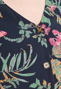 Blusa floreale blu navy con foglie e fiori verdi, rosa e arancioni, dotata di due bottoni in tartaruga vicino al collo.