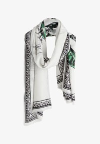 Pañuelo blanco con borde negro ornamentado y patrones de hojas verdes, suelto y drapeado con tela suave y bordes con flecos.