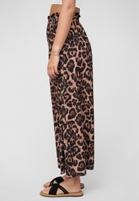 Pantaloni largi cu imprimeu leopard în nuanțe de maro și negru, cu talie elastică, dintr-un material fluid, asortați cu sandale negre.