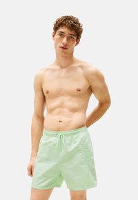 Hellgrüne Badehose aus leichtem Material, mit einem elastischen Bund und Kordelzug sowie dezentem Logo-Detail.