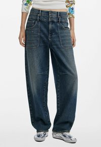 Jeans en denim bleu à jambes larges avec taille haute, présentant une fermeture à double bouton et quatre poches. Le tissu a un effet délavé et une texture lisse.