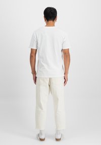 Bílý bavlněný tričko s kulatým výstřihem, spárované s volnými světlobéžovými džíny. Minimalistický design bez viditelných vzorů nebo akcentů.