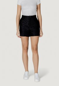 Pantaloni corti neri in pizzo con un motivo floreale, vita alta e chiusura con bottone frontale. Abbinati a una t-shirt bianca aderente a coste e scarpe da ginnastica bianche.