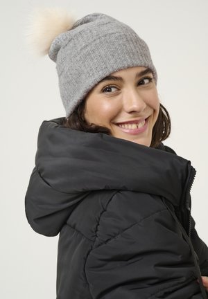 Berretto di lana grigio a maglia con un morbido pom-pom leggero in cima. Indossato con un giubbotto invernale nero con colletto alto e chiusura con zip.
