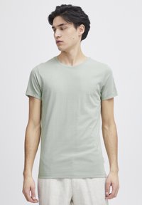 Lys grønn kortermet t-skjorte med rund hals, laget av glatt stoff, med en tettsittende design og et lite merke ved kanten.