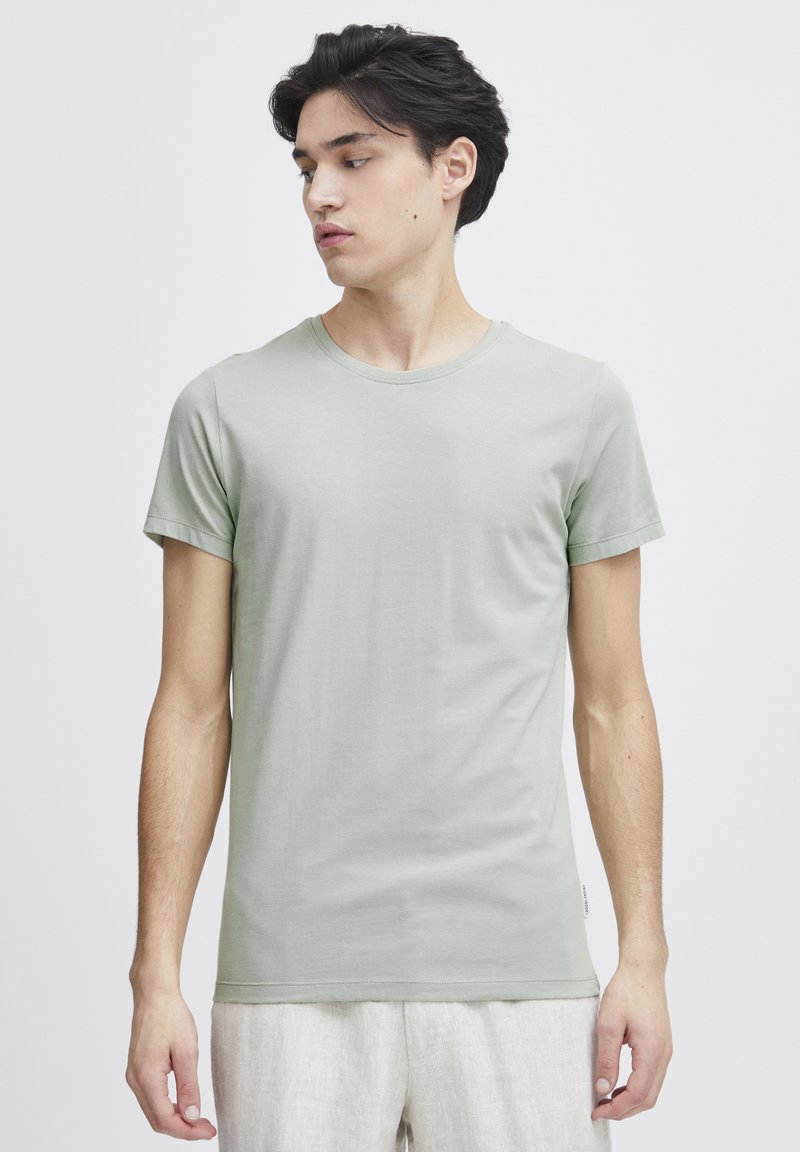 Lys grønn kortermet t-skjorte med rund hals, laget av glatt stoff, med en tettsittende design og et lite merke ved kanten.