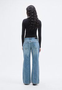 Φαρδιά τζιν παντελόνια σε ανοιχτό γαλάζιο χρώμα με ξεθωριασμένη όψη, διαθέτοντας δύο πίσω τσέπες και μέση μεσαίου ύψους, συνδυασμένα με μαύρο τοπ μακρυμάνικο.