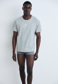 Grå bomull t-skjorte med rund hals og en liten hvit logo detalj på brystet, parret med grå boxershorts.