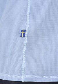Lys blå stof med et struktureret gittermønster, der har hvid syning og et lille svensk flag mærke nær sømmen.