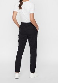 Černé tepláky s elastickým pasem, bočními kapsami a tapered designem. Spárované s fitted bílým tričkem a bílými teniskami.