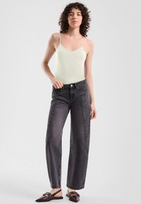 Hellgrün gemusterter Tanktop, hochgeschnittene, dunkelgraue, weite Jeans und dunkelbraune Slipper mit dekorativen Hardware-Akzenten.